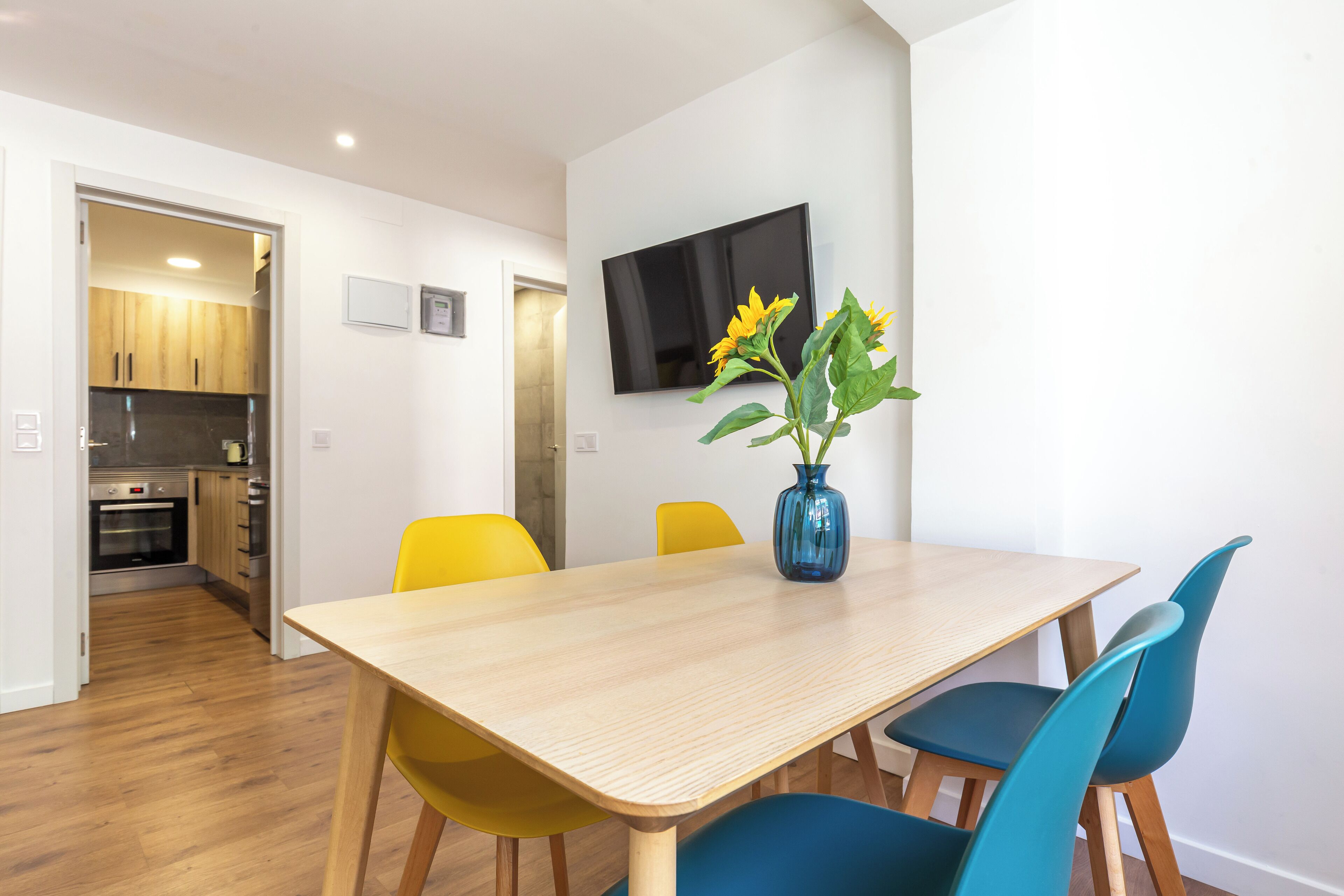 A dining area with a wooden table, yellow and blue chairs, and a vase with flowers.