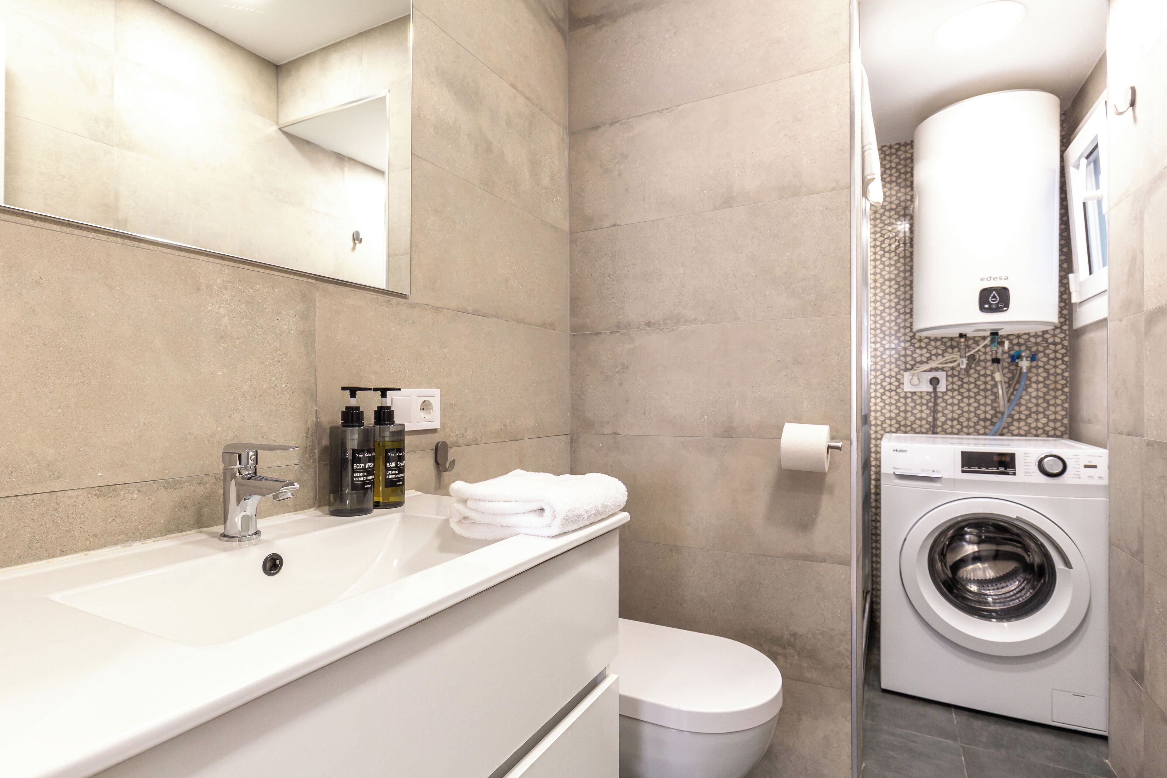 A modern bathroom with a white sink, toilet, and a built-in washing machine.