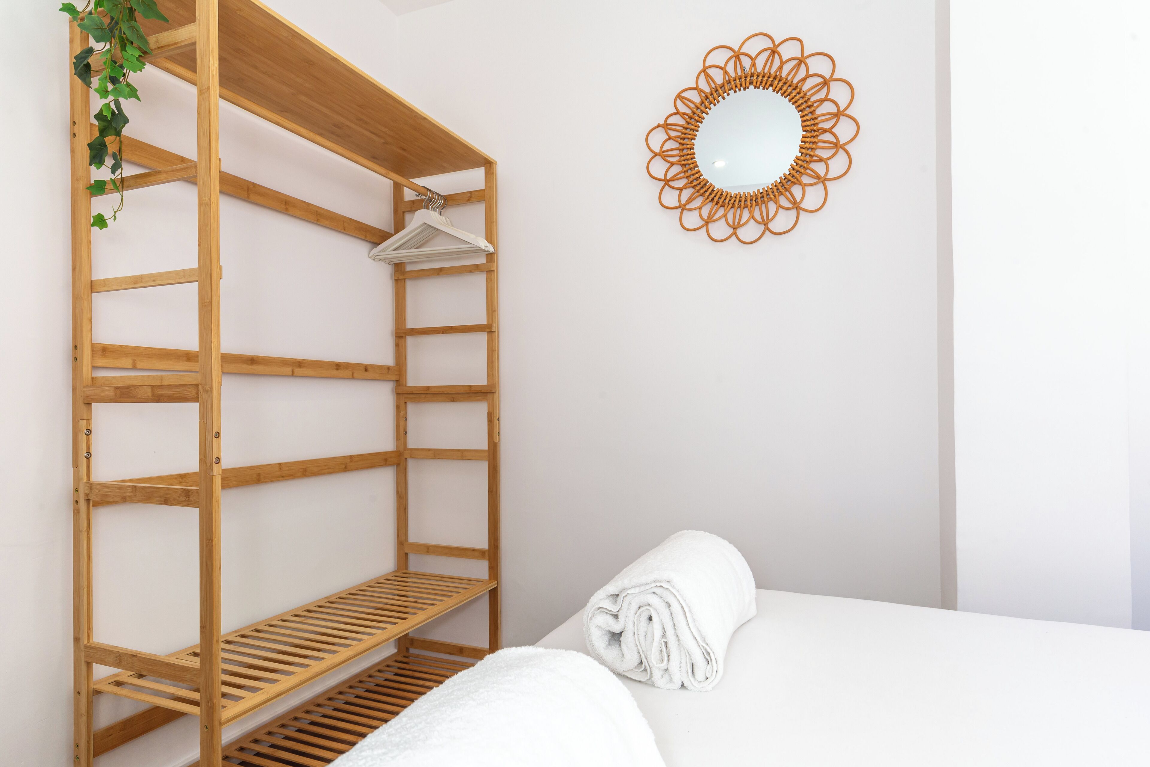 Une étagère en bois avec un porte-serviettes suspendu, une serviette blanche roulée et un miroir décoratif accroché au mur.