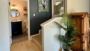 A modern interior with a staircase leading to a second floor, a wooden cabinet, and a potted plant. - Beach Retreat: Walk to Beach & Pool, Sleeps 12, Pet Friendly (Port Aransas)