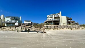A beachfront property with a wooden staircase leading to a balcony, a large building with multiple balconies, and a sign indicating 'Lost Colony Villas'. - Beach Retreat: Walk to Beach & Pool, Sleeps 12, Pet Friendly (Port Aransas)