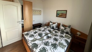 A bedroom with a bed, a wooden wardrobe, a bench, a small table with a lamp, and a picture on the wall. - Apartment near the beach in the city center  (Rerik)