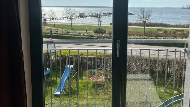 A view from a balcony with a metal railing, overlooking a body of water, a dock, and a playground with slides. - Apartment near the beach in the city center  (Rerik)