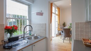 A kitchen with a sink, a vase of red flowers, and a window with curtains. - 3 bed House Camberwell With Private Garden (London)