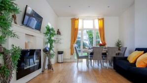 A modern living room with a flat-screen TV, a sofa, and a dining area with chairs and a table. - 3 bed House Camberwell With Private Garden (London)