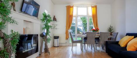 Ein modernes Wohnzimmer mit Flachbildfernseher, einer Couch und einem Essbereich mit Stühlen und Tisch.
