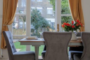 A dining area with a table set for two, a vase of red flowers, and a bottle of champagne. - 3 bed House Camberwell With Private Garden (London)