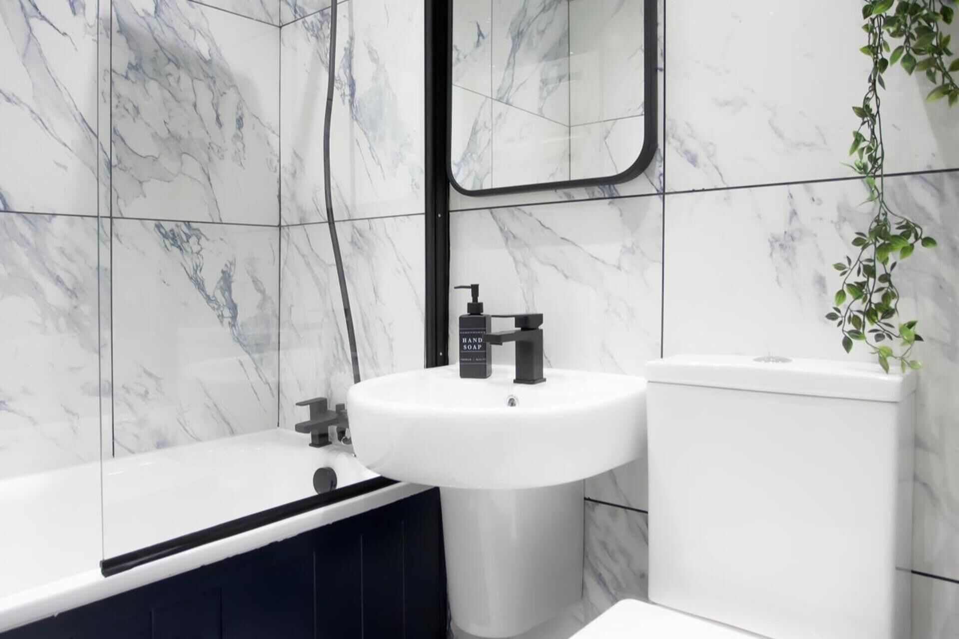 A bathroom with a white sink, a black faucet, a white toilet, and a black bathtub.