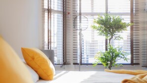 A hotel room with a bed, a window with blinds, a small plant, and a yellow pillow. - 3 bed House Camberwell With Private Garden (London)