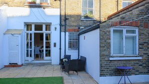 A small patio with a lawn, a table, and chairs. - 3 bed House Camberwell With Private Garden (London)