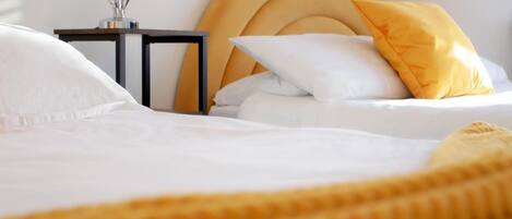 Ein ordentlich gemachtes Bett mit weißen Leinen und einer gelben Tagesdecke.