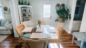Un coin repas avec une table en verre, des chaises en osier et un lustre orné d’abat-jours rouges.