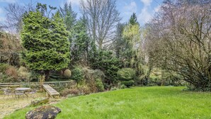 Un jardin bien entretenu, agrémenté de divers arbres, d’un banc en pierre et d’une pelouse verdoyante.