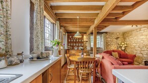 Une cuisine rustique avec des poutres en bois, un mur en pierre et un coin salon accueillant avec un canapé rouge.