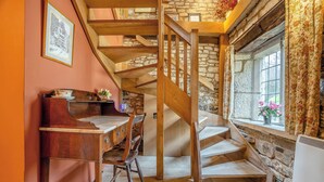Un intérieur rustique avec un escalier en bois, des murs en pierre, un bureau en bois avec des chaises et une fenêtre avec des rideaux.
