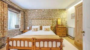 Une chambre avec un mur en pierre, un cadre de lit en bois, une commode et un miroir.