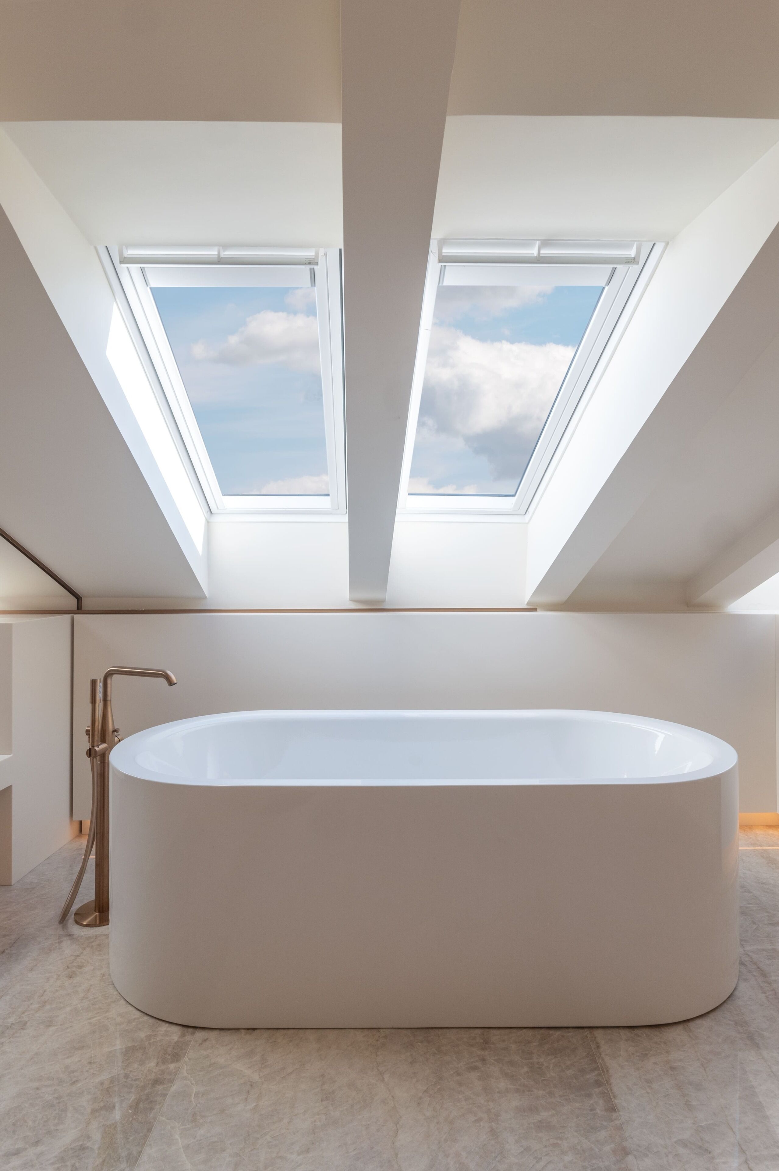 A modern bathroom with a freestanding bathtub, skylights, and a marble floor.