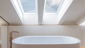 A modern bathroom with a freestanding bathtub, skylights, and a marble floor.