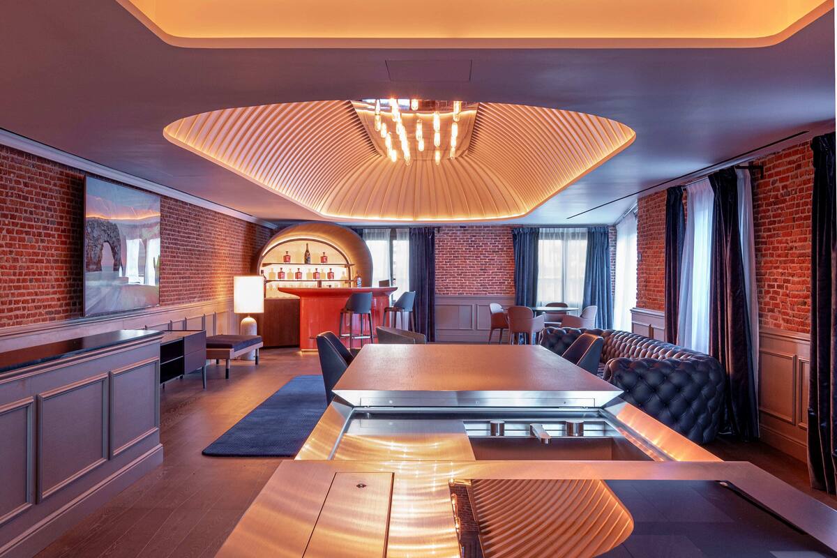 A modern dining area with a long table, cushioned seating, and a unique ceiling light fixture.