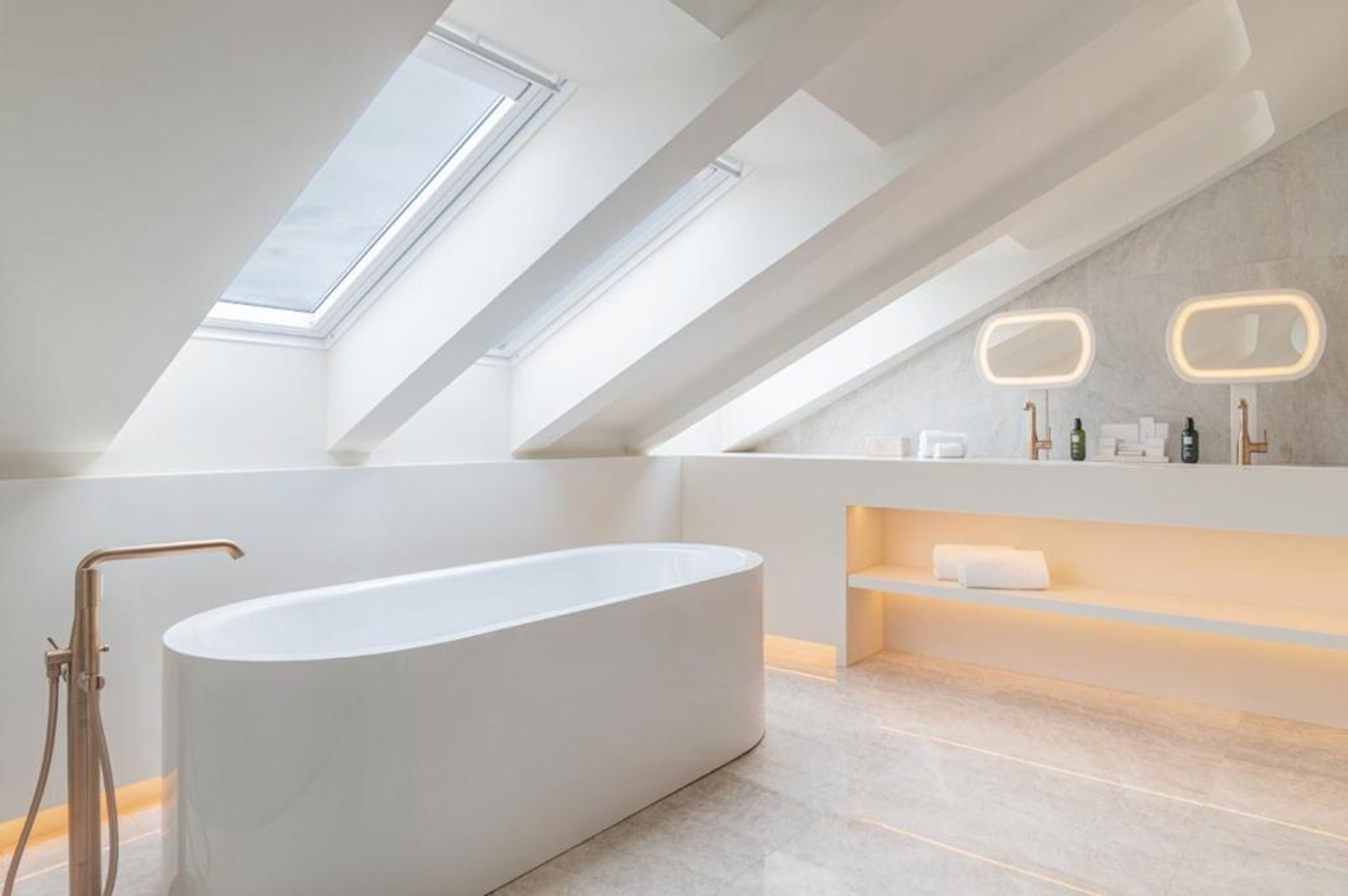 Ein modernes Badezimmer mit freistehender Badewanne, Dachfenstern und einem Waschtisch mit beleuchteten Spiegeln.