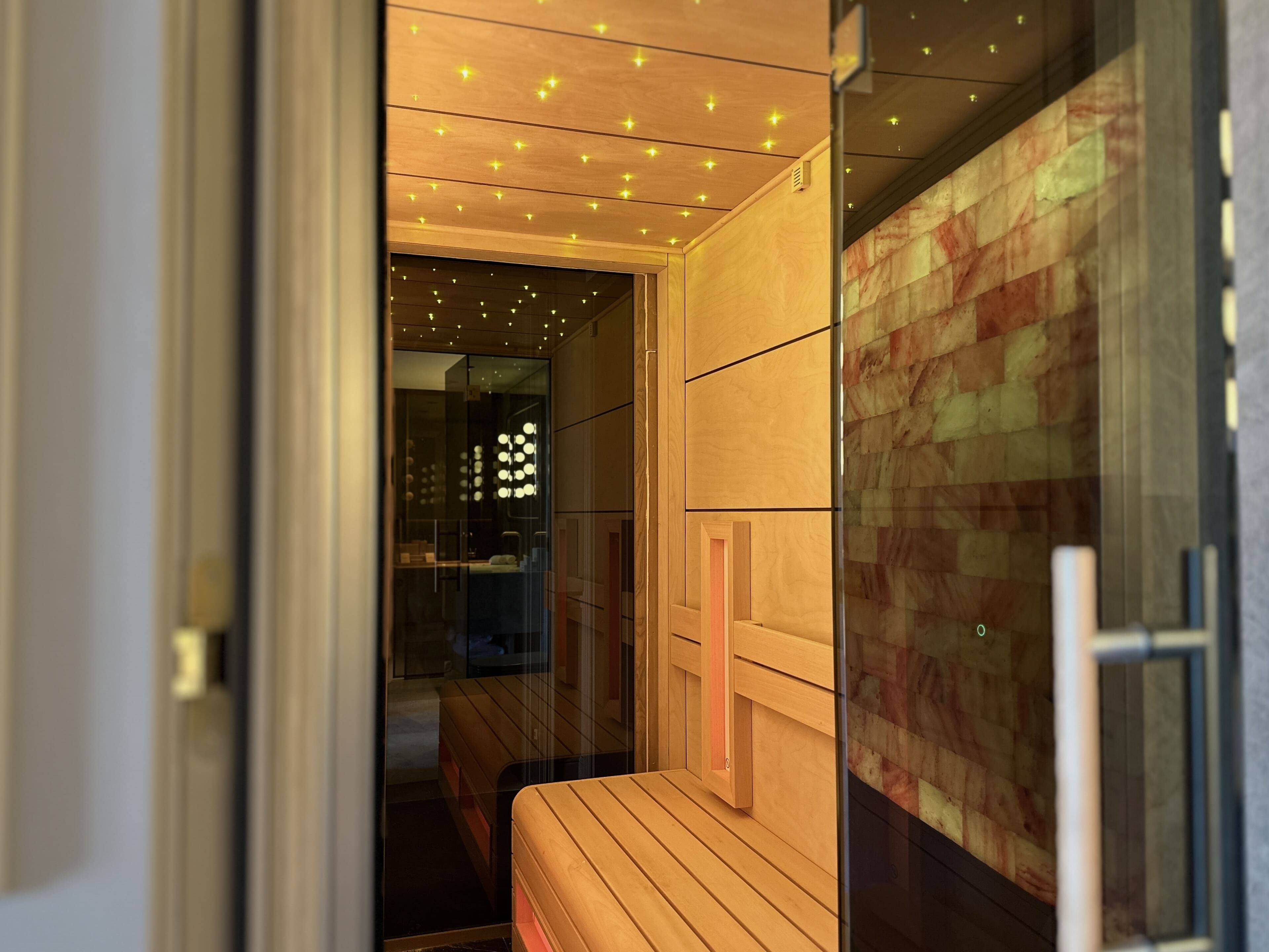 A modern bathroom with a wooden vanity, a glass shower enclosure, and a patterned wall.