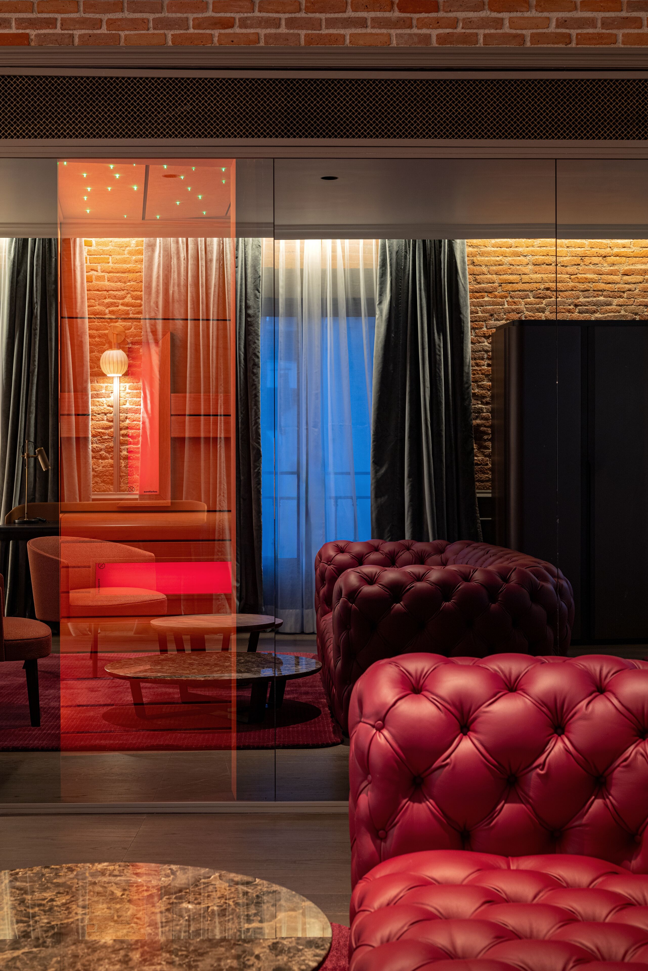A modern living room with a red leather sofa, a round coffee table, and a glass partition.
