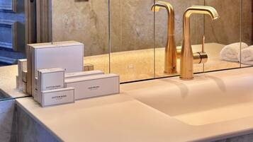 Un baño con encimera de mármol, grifo dorado y un espejo que refleja una pared azul y luces.