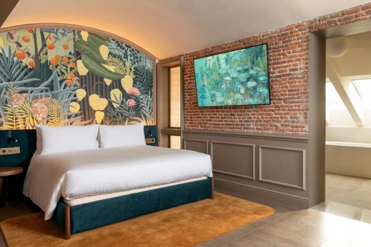 A bedroom with a large bed, a mural on the wall, a TV, and a brick wall.