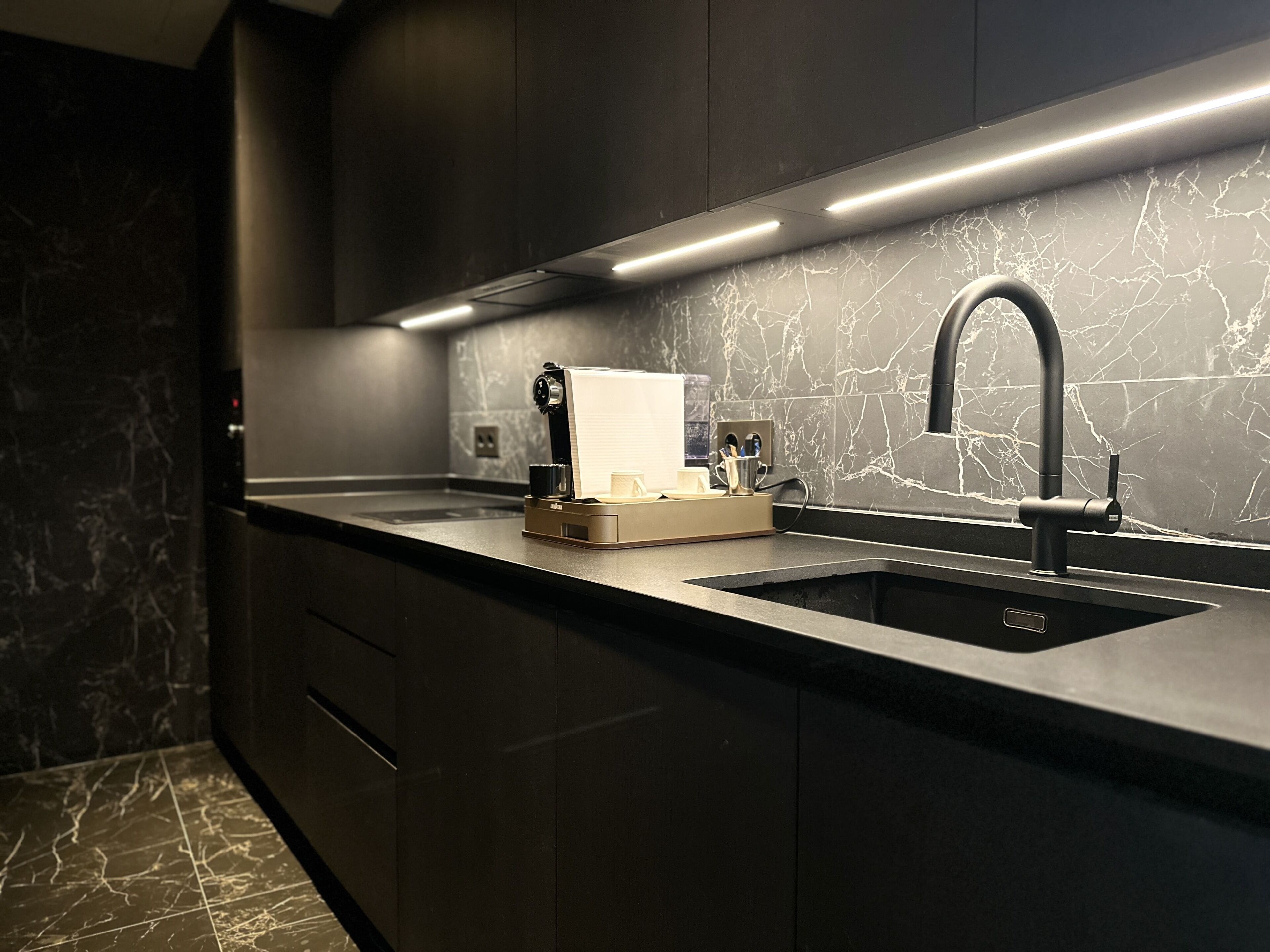 Eine moderne Küche mit dunklen Schränken, einer Marmor-Spritzschutzwand und einem Edelstahl-Spülbecken.