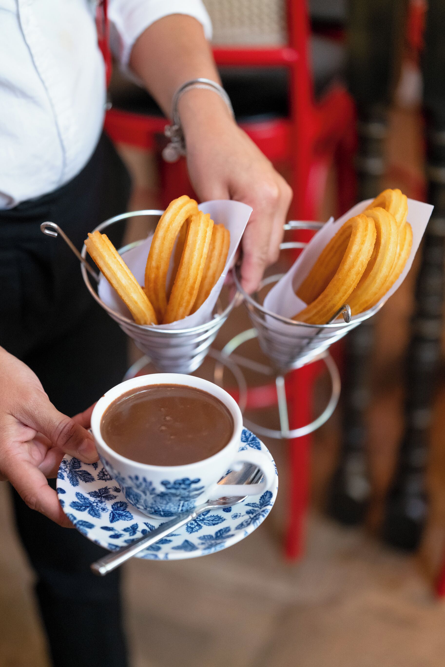 Una persona sosteniendo una bandeja con churros y una taza de chocolate caliente.