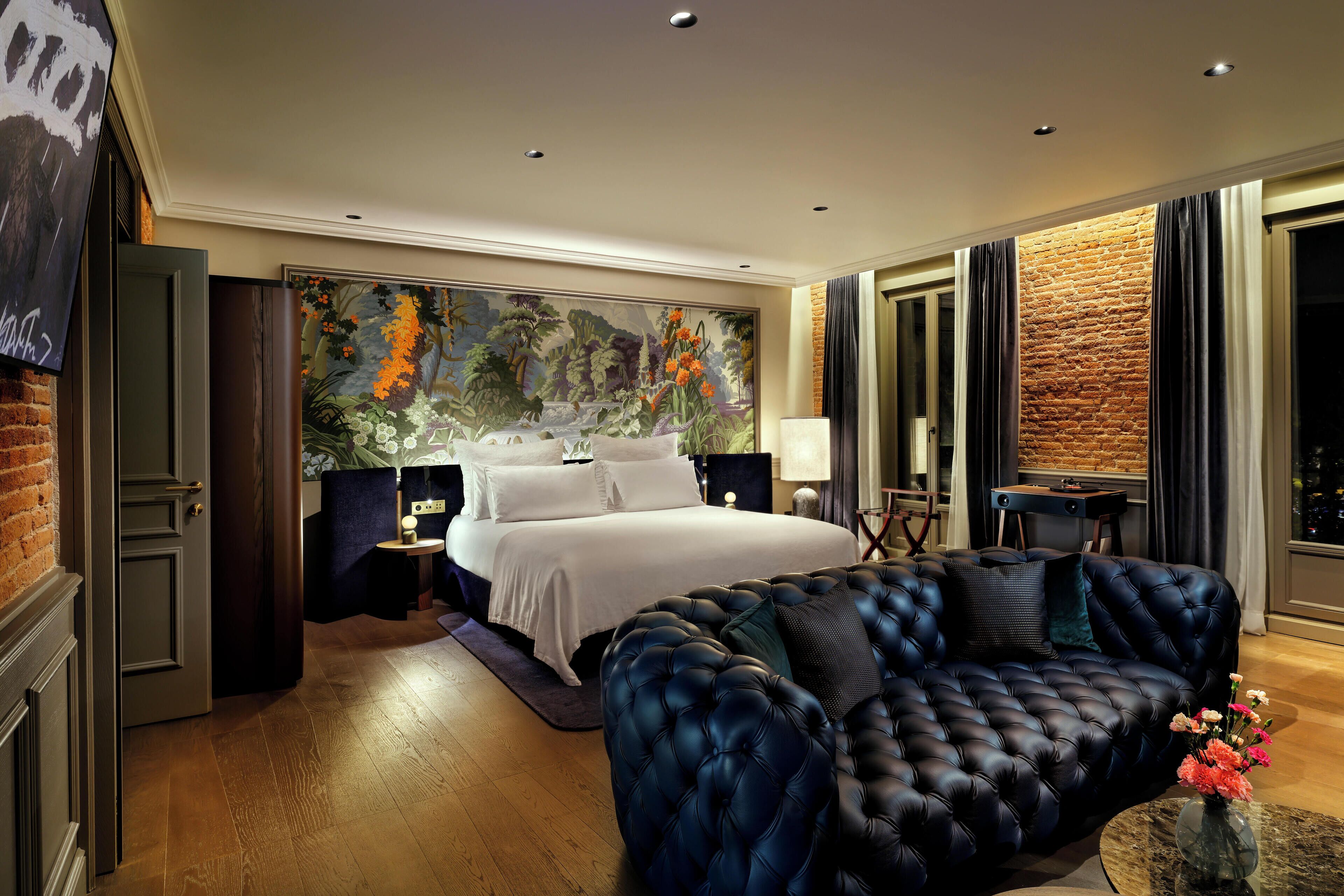 Un dormitorio con una cama grande, un sofá azul oscuro, un cuadro en la pared y una pared de ladrillo decorativa.