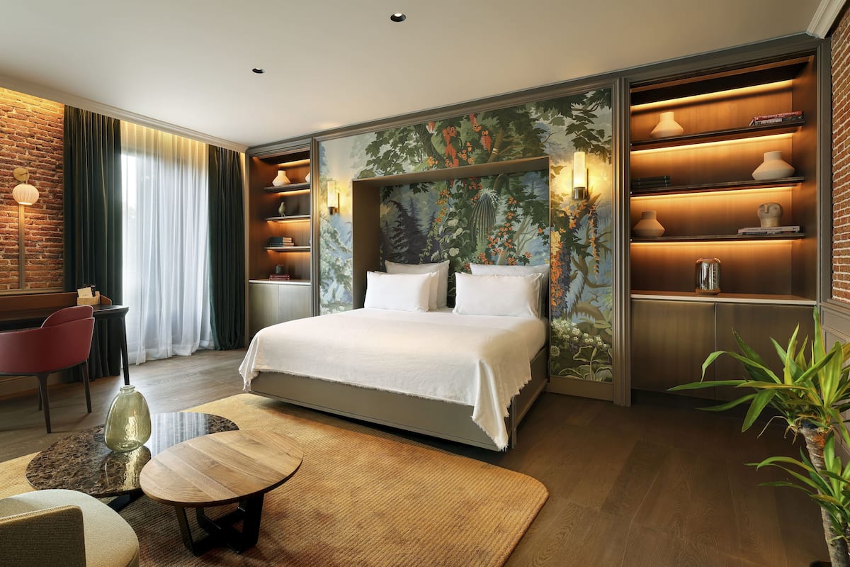 A modern hotel room with a large bed, a desk, and a bookshelf.