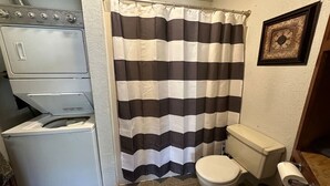 Ein kleines Badezimmer mit einer gestreiften Duschvorhang, einer Toilette und einer gestapelten Waschmaschine und einem Trockner.