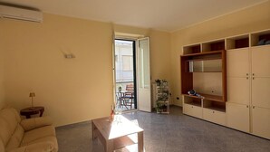 Ein Wohnzimmer mit einer Couch, einem Couchtisch, einer TV-Kommode und einer Tür, die auf einen Balkon führt.
