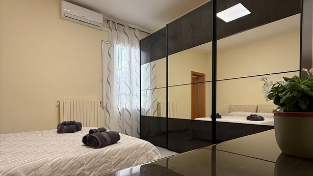 Ein modernes Schlafzimmer mit großem Spiegel, einem Bett mit gerollten Handtüchern, einem Heizkörper und einer Topfpflanze.