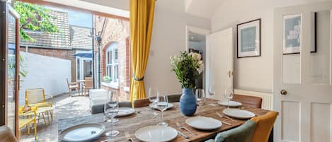 Un comedor con una mesa de madera dispuesta para cuatro, un florero y vistas al exterior.