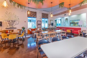 L’intérieur d’un café, avec des tables, des chaises et une enseigne murale indiquant : « The Palms Coffee House ».