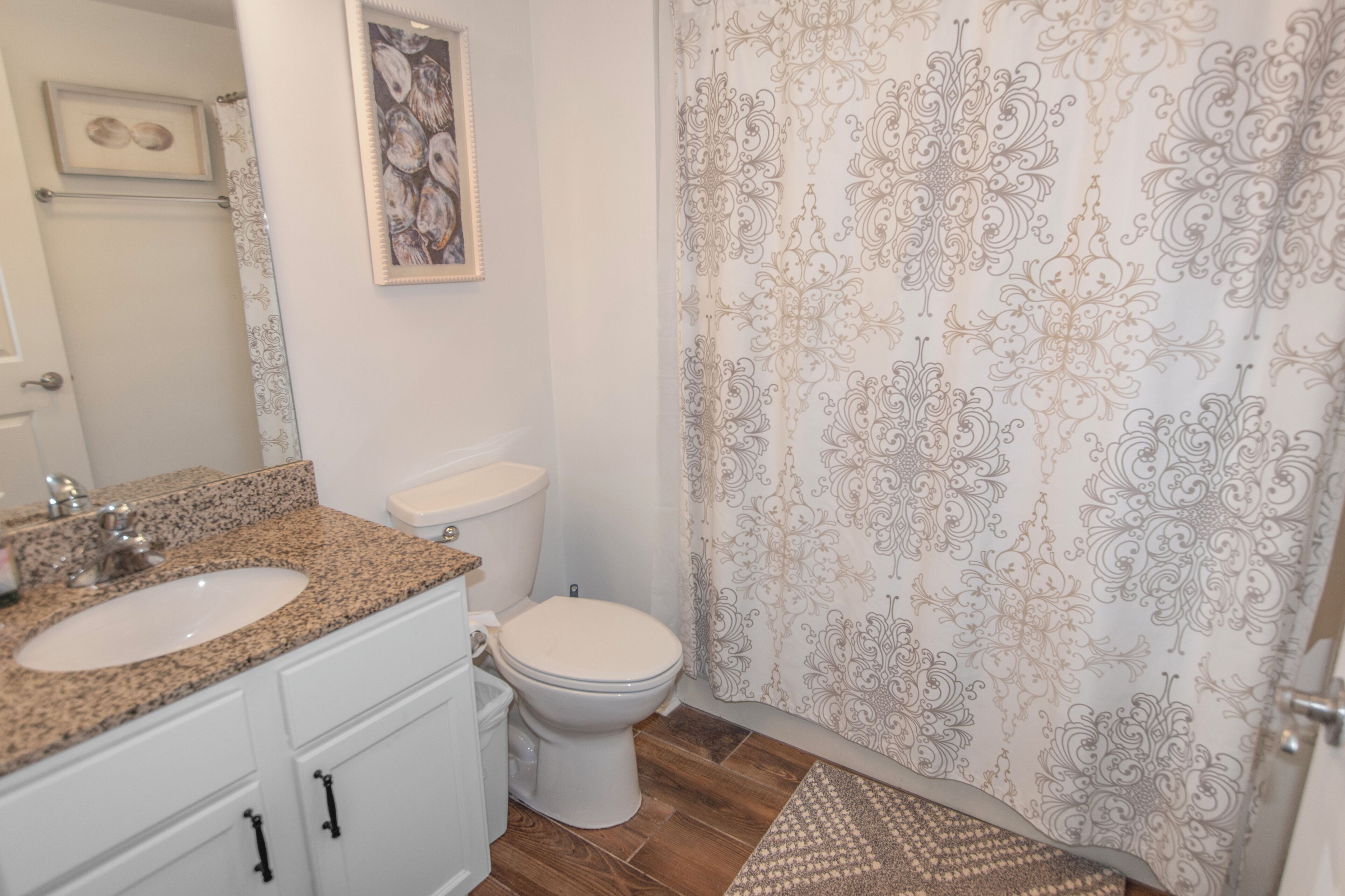 Een badkamer met een wastafel met granieten blad, een toilet en een douchegordijn met een bloemenmotief.