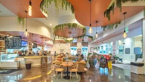 A modern coffee shop with a central seating area, a counter with a menu board, and hanging plants. - 🌴The Palms of Destin 1411 - The Pretty Palm | Easy Beach Access | Great Views🌴 (Destin)