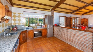 A kitchen with a brick wall, wooden beams, a stainless steel refrigerator, and a window with a view of greenery. - Villa Casa Tania by Villa Plus (Frigiliana)