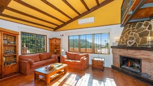 A spacious living room with a fireplace, wooden furniture, and large windows offering a view of the outdoors. - Villa Casa Tania by Villa Plus (Frigiliana)