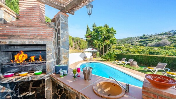 A poolside area with a stone fireplace, a pool, and lounge chairs. - Villa Casa Tania by Villa Plus (Frigiliana)