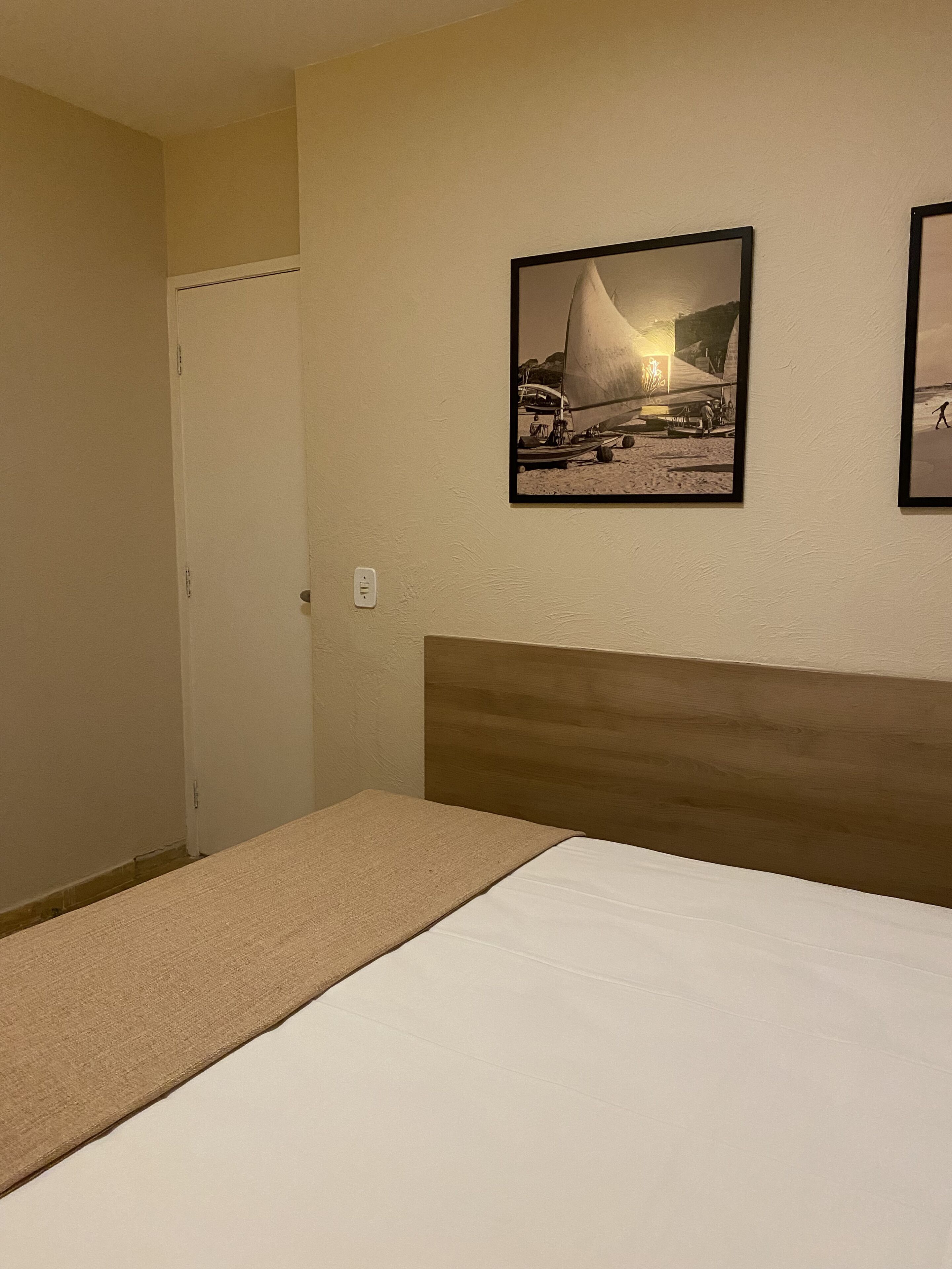 Una habitación de hotel con una cama, un cabecero y dos cuadros en la pared.