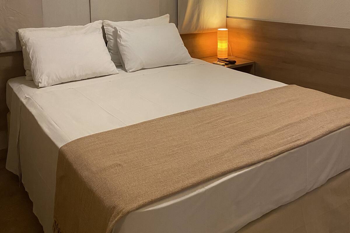 Ein Hotelzimmer mit einem großen Bett, einem Nachttisch mit Lampe und einem Vorhangverhang am Kopfteil.