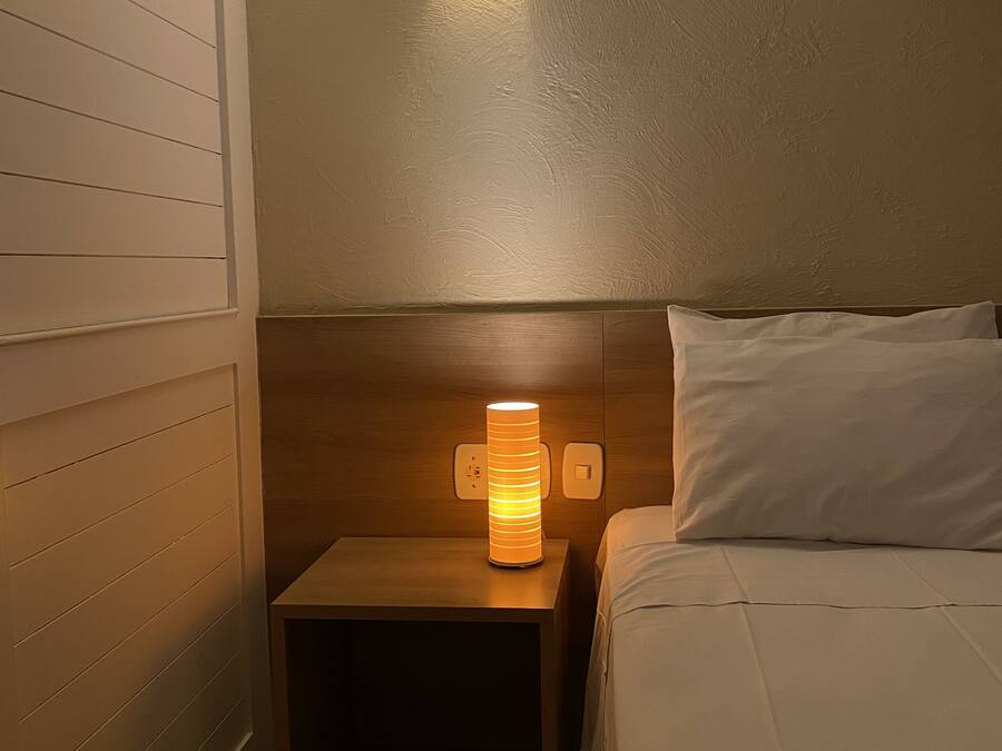 Un dormitorio con una mesita de noche, una lámpara de pared, una cama y un aire acondicionado instalado en el techo.