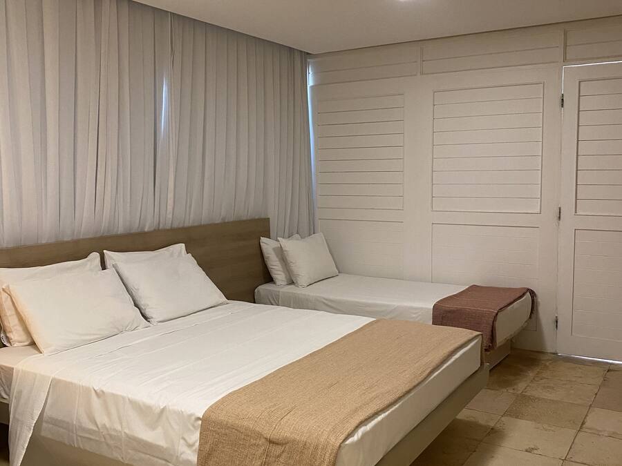 A hotel room with two beds, a large window with curtains, a wardrobe, and a tiled floor.