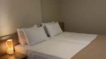 A neatly made bed with white linens, a wooden nightstand with a lamp, and a brown throw blanket.