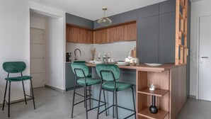 A modern kitchen with wooden cabinets, a bar area with green bar stools, and a small shelf with a vase. - Apartment for 4, center and seaside (Saint-Brevin-les-Pins)