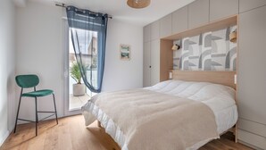 A bedroom with a bed, a chair, a window with curtains, and a wall with a geometric pattern. - Apartment for 4, center and seaside (Saint-Brevin-les-Pins)