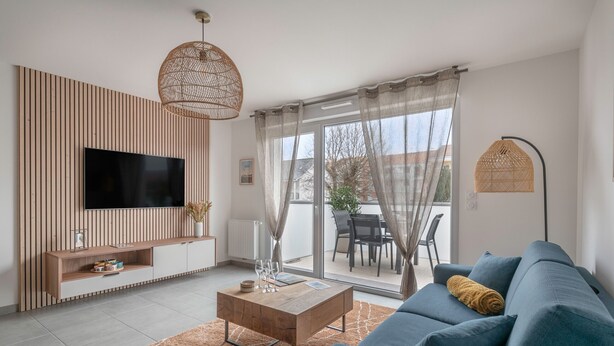 A modern living room with a flat-screen TV, wooden panel wall, and a blue sofa. - Apartment for 4, center and seaside (Saint-Brevin-les-Pins)